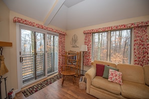 Un salon chaleureux avec un plancher en bois, un canapé beige agrémenté de coussins à motifs floraux, une chaise en bois et une bibliothèque.
