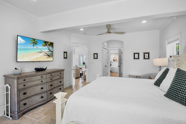A bedroom with a large bed, a dresser, a TV on the wall, and a ceiling fan.
