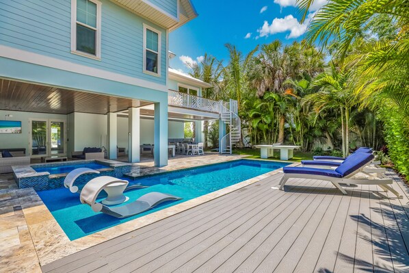Una casa moderna con piscina, mobiliario de exterior y un porche cubierto.