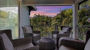 A balcony with wicker furniture and a view of palm trees and a sunset.