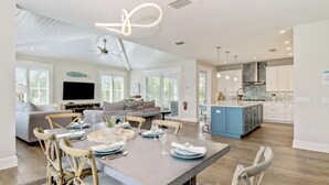 A spacious living area with a dining table set for six, a kitchen with blue cabinets, and a large window providing natural light.