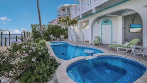 Un espace piscine comprenant deux piscines, des chaises longues et un escalier menant à un bâtiment doté de balcons.