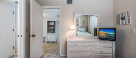 Un dormitorio con cama, cómoda, televisor y puerta que da a otra habitación.