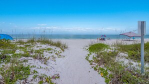 A beach path leading to the ocean with a tent and umbrellas in the background.