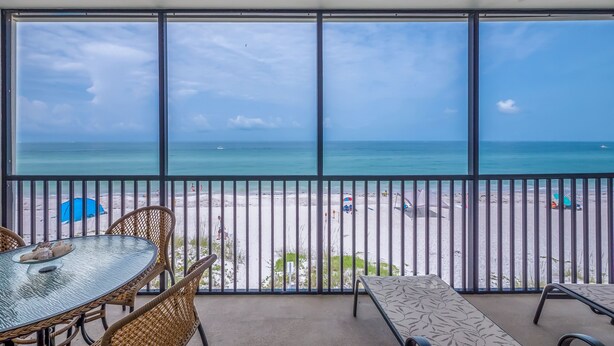A balcony with a view of the beach, wicker chairs, a table, and a patterned bench.
