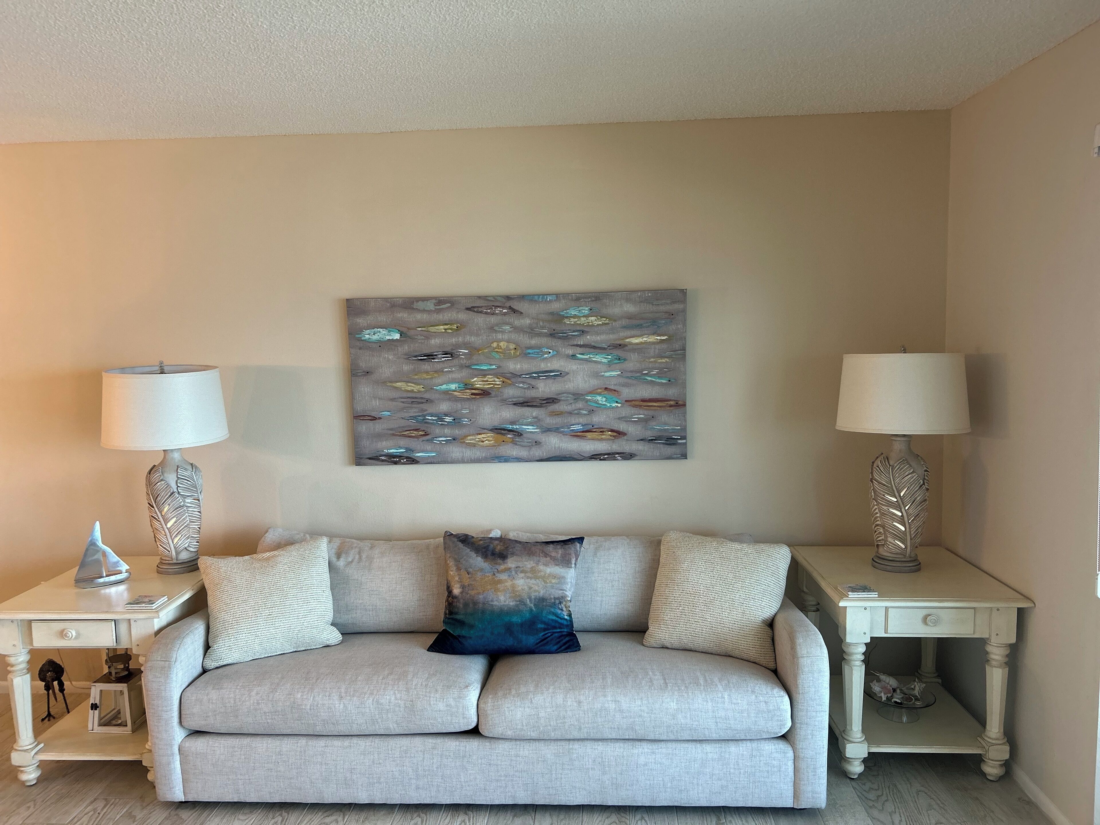 A living room with a beige sofa, two side tables with lamps, and a wall-mounted abstract painting.