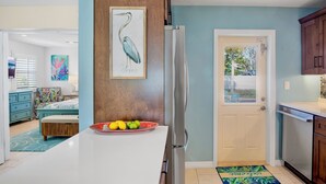 Una cocina moderna con un refrigerador grande, una zona de comedor con una mesa blanca y una puerta que da a un balcón.