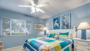 Un dormitorio con cama, mesita de noche, cómoda, ventilador de techo y una obra de arte en la pared.