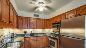 Una cocina con armarios de madera, un refrigerador de acero inoxidable, un microondas y un ventilador de techo.