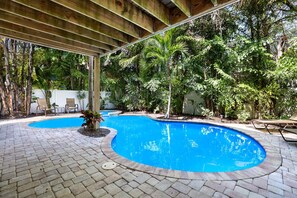A swimming pool with a brick deck, surrounded by lush greenery and trees. - Beautiful home with fenced yard, heated pool, hot tub, and elevator! (Holmes Beach)