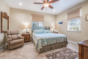 A bedroom with a bed, a recliner, a ceiling fan, and a window with blinds. - Beautiful home with fenced yard, heated pool, hot tub, and elevator! (Holmes Beach)