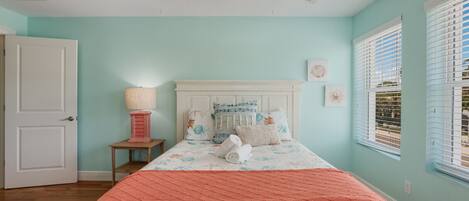 A bedroom with a bed, a ceiling fan, a nightstand with a lamp, and a window with blinds.
