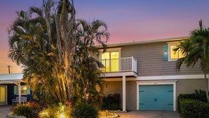 A two-story house with a balcony, a garage, and a well-lit driveway. - Coastal Home with Heated Pool, Close to Beach! (Holmes Beach)