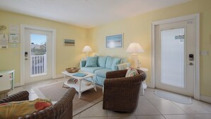 A living room with a light blue sofa, two lamps, a wicker chair, a small table, and a white coffee table. - Coastal Home with Heated Pool, Close to Beach! (Holmes Beach)