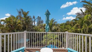 A deck with a white railing, a small table, and blue chairs. - Coastal Home with Heated Pool, Close to Beach! (Holmes Beach)