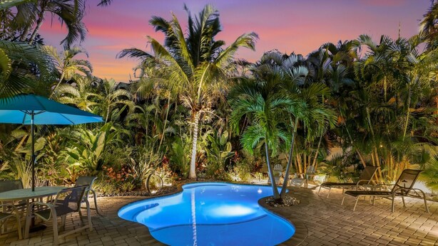 A pool surrounded by palm trees and a sunset sky. - Coastal Home with Heated Pool, Close to Beach! (Holmes Beach)