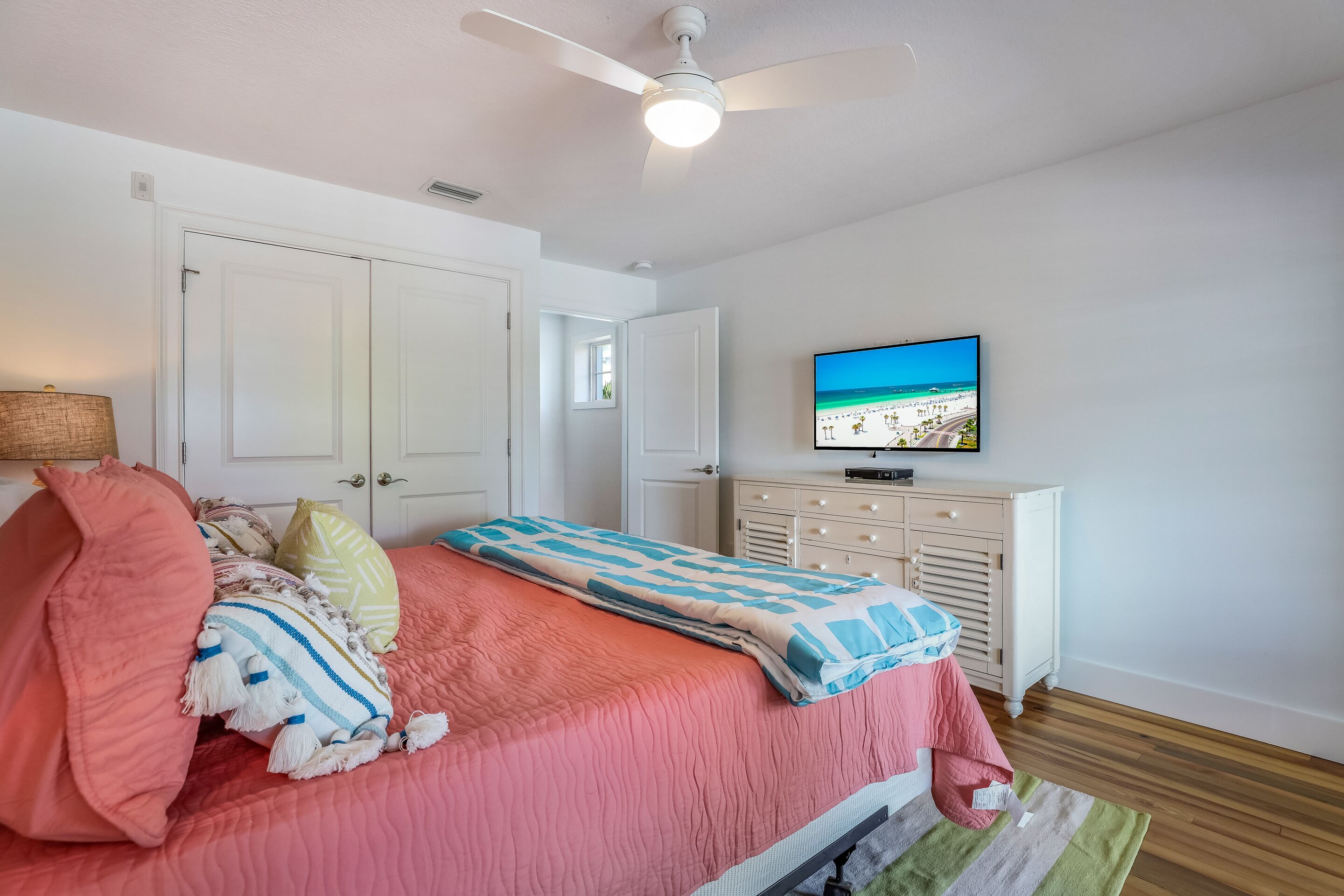 A bedroom with a bed, a ceiling fan, a television, and a dresser.