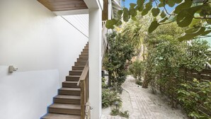 Un escalier menant à un espace extérieur abrité, avec un chemin en briques et de la verdure.