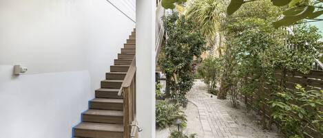 A staircase leading to a covered outdoor area with a brick pathway and greenery.