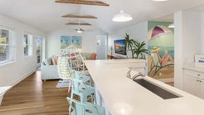 Une cuisine moderne dotée d’un îlot central, de poutres en bois au plafond et d’un coin repas avec des chaises bleu clair.