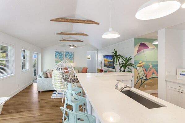 A modern kitchen with a central island, wooden beams on the ceiling, and a dining area with light blue chairs.