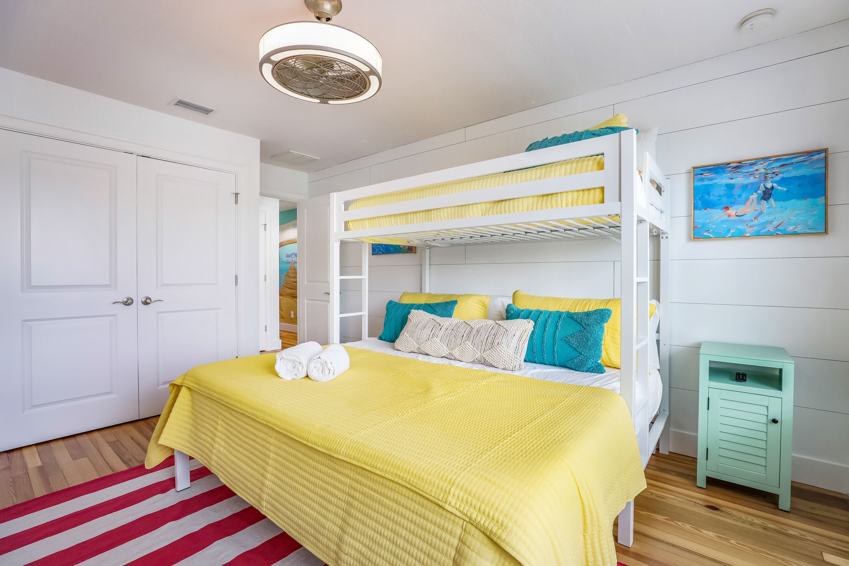 A bunk bed room with a yellow bedspread, white walls, and a painting on the wall.