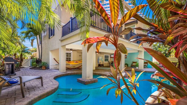 A pool area with a hammock, lounge chairs, and a view of a building with balconies. - Perfect Vacation Home! Pool, Lounge, and Ping Pong (Holmes Beach)