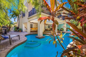 A pool area with a hammock, lounge chairs, and a view of a building with balconies. - Perfect Vacation Home! Pool, Lounge, and Ping Pong (Holmes Beach)