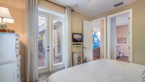 A bedroom with a bed, a dresser, a television on a stand, and a door leading to another room. - Perfect Vacation Home! Pool, Lounge, and Ping Pong (Holmes Beach)