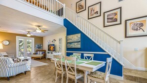 A spacious living area with a dining set, a staircase, and artwork on the walls. - Perfect Vacation Home! Pool, Lounge, and Ping Pong (Holmes Beach)