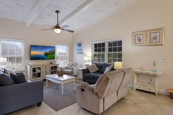 A spacious living room with a ceiling fan, a flat-screen TV, and a comfortable seating area with a sofa and armchairs.