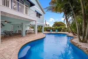 A swimming pool with a curved edge, surrounded by a patio area with chairs and tables.