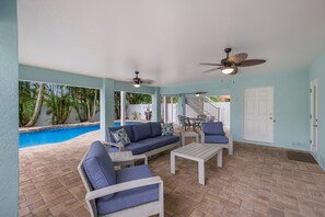 A covered outdoor area with a pool, blue and white furniture, ceiling fans, and a staircase leading to an upper level. - Beautifully outfitted home with a heated pool and tropical backyard! (Holmes Beach)