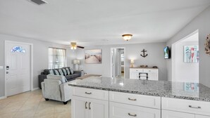 A spacious kitchen with white cabinetry, granite countertops, and a dining area with a gray sofa. - Island Mojo! Family-Friendly Beach Escape! (Holmes Beach)