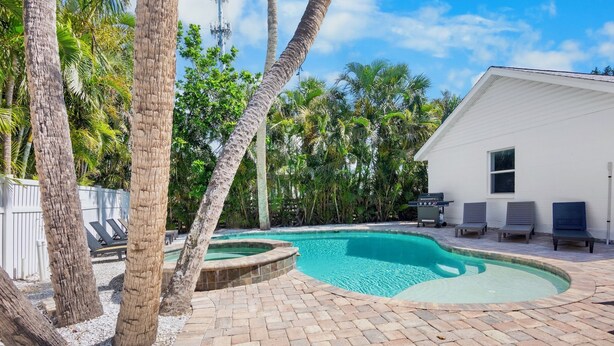 A swimming pool with a curved edge, surrounded by palm trees and a white building. - Island Mojo! Family-Friendly Beach Escape! (Holmes Beach)