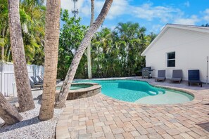 A swimming pool with a curved edge, surrounded by palm trees and a white building. - Island Mojo! Family-Friendly Beach Escape! (Holmes Beach)