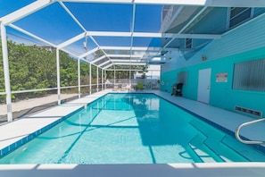 Une piscine d’un bleu éclatant, avec une terrasse blanche et un espace abrité.