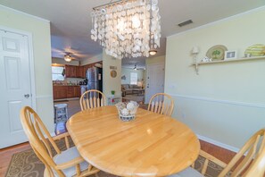 Un coin repas avec une table et des chaises en bois, un lustre et une cuisine en arrière-plan.