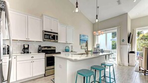 A modern kitchen with white cabinetry, a central island with bar stools, and a view of the outdoors. - Villa with Heated Pool and Swim-up Tiki Bar! Close to Beach - La Mer (Holmes Beach)