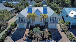A large, two-story house with a blue roof, surrounded by palm trees and a paved driveway. - Villa with Heated Pool and Swim-up Tiki Bar! Close to Beach - La Mer (Holmes Beach)