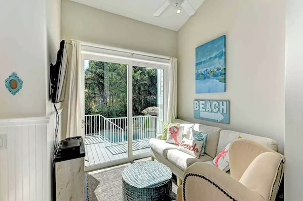 A living room with a sliding glass door leading to a balcony, a sofa with decorative pillows, a mounted TV, and a painting on the wall.