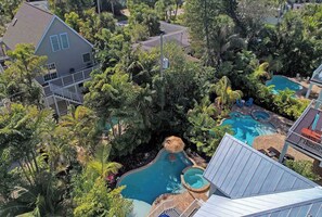 A residential area with a large swimming pool surrounded by lush greenery and a house with a balcony.