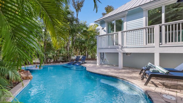 Piscina com espreguiçadeiras e um edifício branco com varanda.