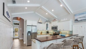 Cozinha moderna com armários brancos, geladeira de aço inoxidável, micro-ondas e uma ilha grande com banquetas.
