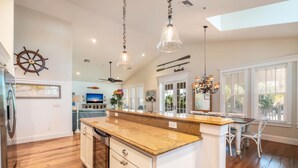 A spacious kitchen with a central island, wooden flooring, and pendant lighting. - Cozy Pine Ave Cottage Near Beach (Anna Maria)