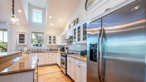 A modern kitchen with white cabinets, stainless steel appliances, and a wooden floor. - Cozy Pine Ave Cottage Near Beach (Anna Maria)