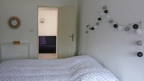 Um quarto com cama, cómoda, porta que dá para outro espaço, decoração na parede e uma guirlanda de enfeites esféricos.