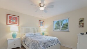 A bedroom with a bed, two bedside tables with lamps, a ceiling fan, and a window with blinds. - Beautiful Condo with Pool, Just Steps to the Beach! (Holmes Beach)