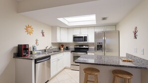 A modern kitchen with white cabinets, stainless steel appliances, a skylight, and a bar area with stools. - Beautiful Condo with Pool, Just Steps to the Beach! (Holmes Beach)