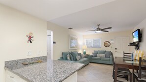 A kitchen with a granite countertop, a dining area with a table and chairs, a ceiling fan, and a television mounted on the wall. - Beautiful Condo with Pool, Just Steps to the Beach! (Holmes Beach)